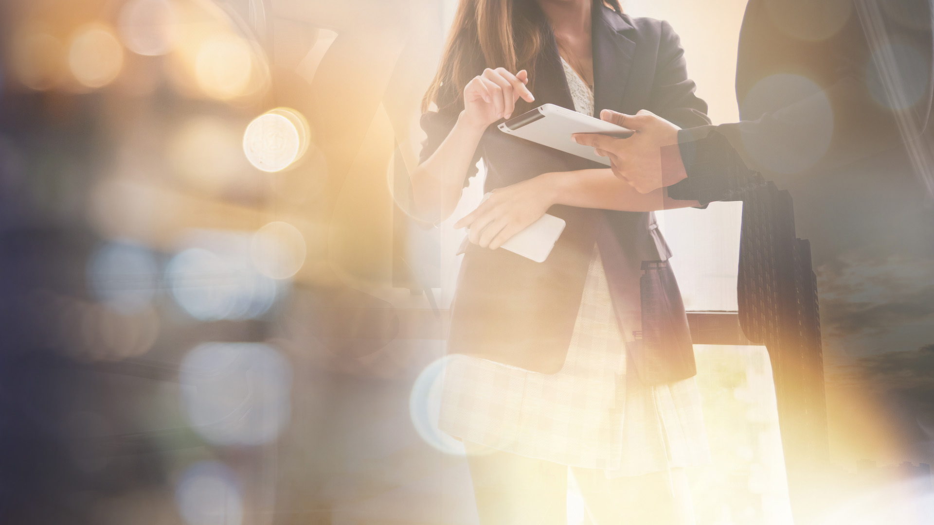 Abstract image of lights with business partners hands discussing over a tablet